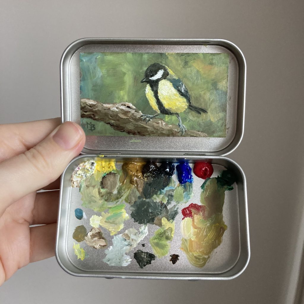 Blikvanger miniatuur schilderij in blikje met bijbehorende originele palet van koolmees op tak met groene achtergrond