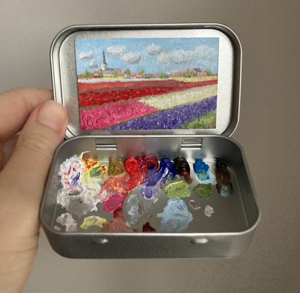 Blikvanger miniatuur schilderij in blikje met bijbehorende originele palet van bollenvelden met witte kerk Noordwijkerhout in de verte