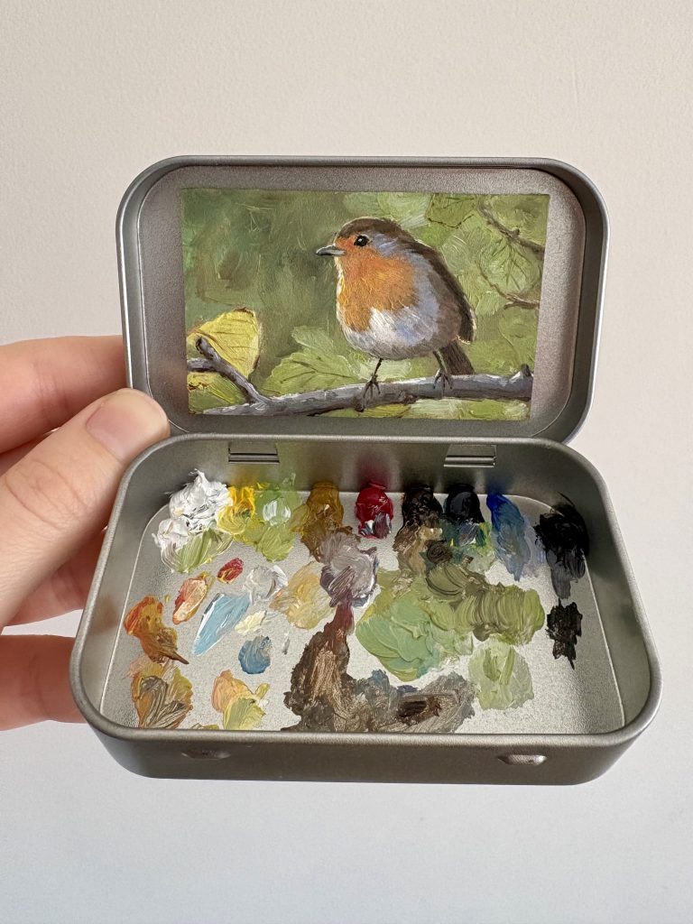 Blikvanger miniatuur schilderij in blikje met bijbehorende originele palet van roodborstje op tak met blaadjes groene achtergrond