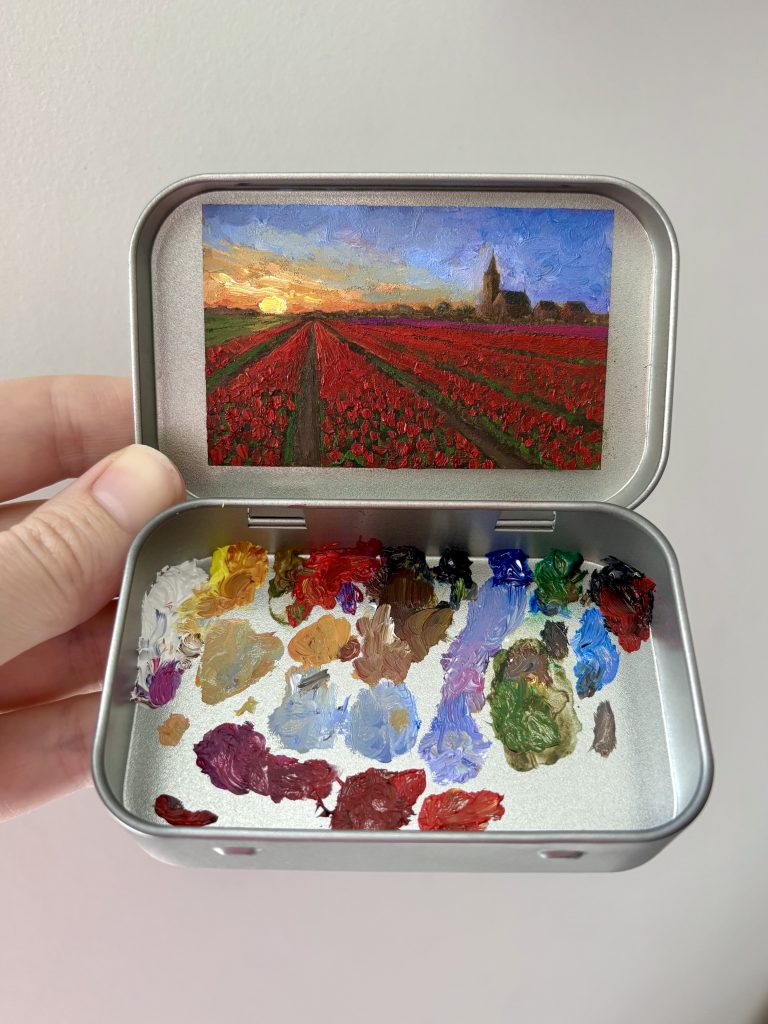 Blikvanger miniatuur schilderij in blikje met bijbehorende originele palet van bollenvelden met rode tulpen bij zonsondergang bij de Zilk